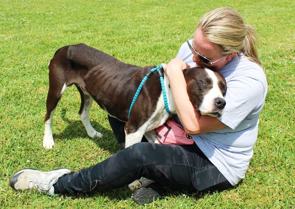 Photo of a woman hugging a dog in the grass.